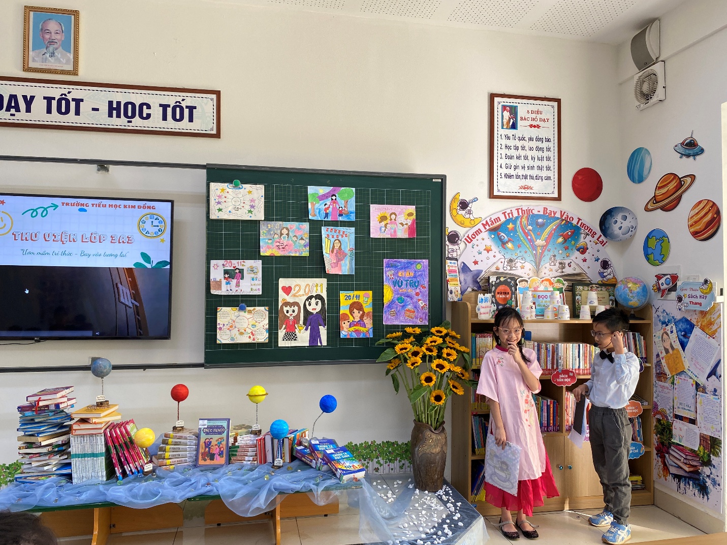 A room with a table and a table with books and a table with a bookcase and a couple of kids
Description automatically generated with medium confidence