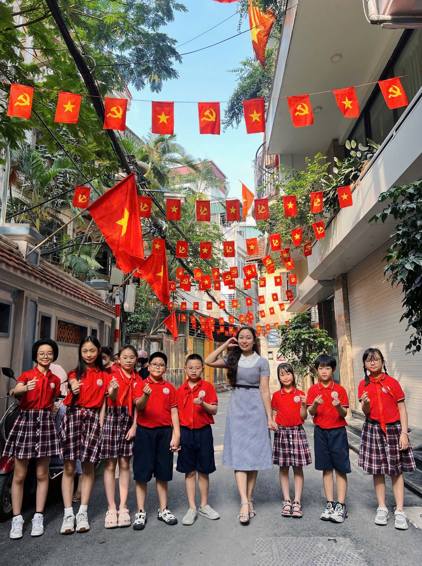 A group of children and a person standing in a street with flags
Description automatically generated