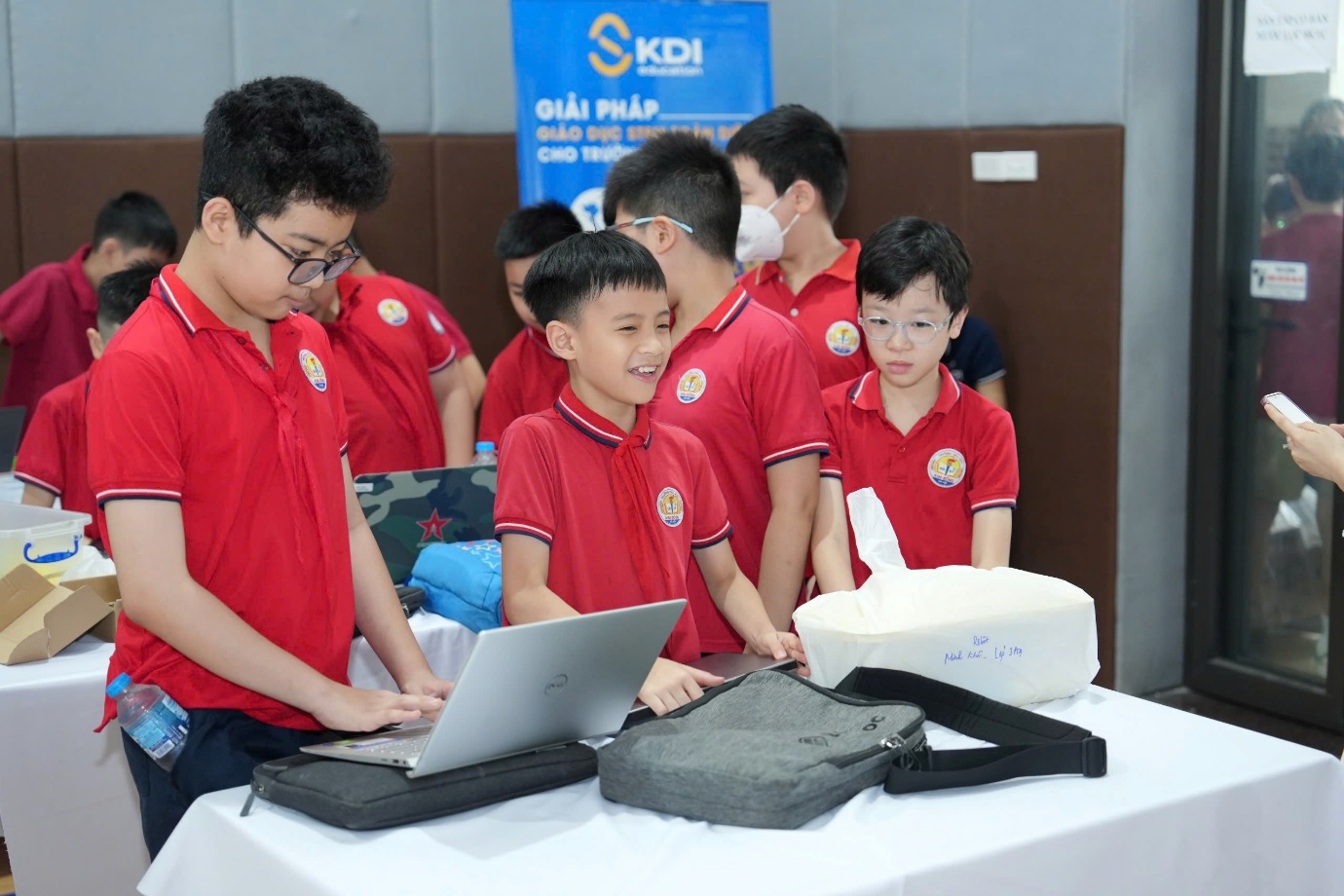 A group of boys in red shirts standing around a table with laptopsAI-generated content may be incorrect.
