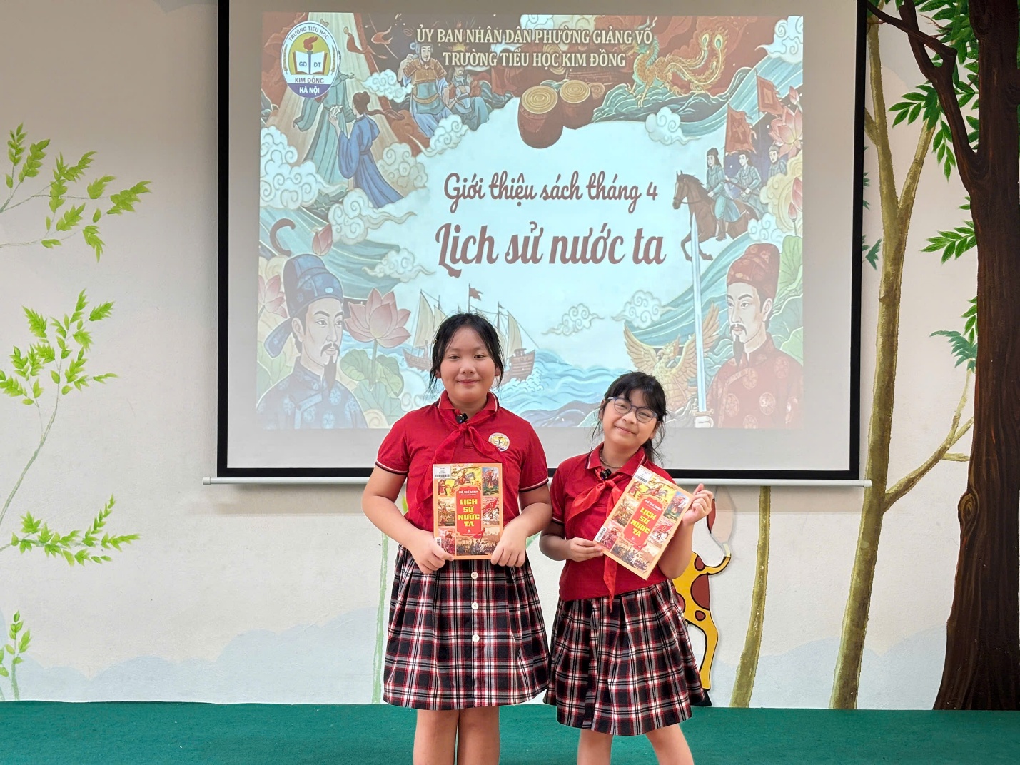Two girls holding books in front of a screen
Description automatically generated